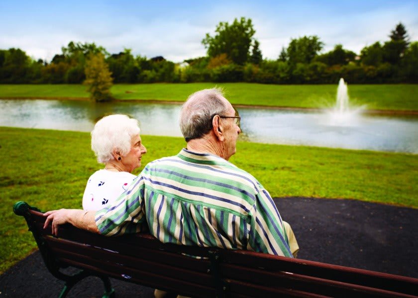 An elderly couple sitting on a bench by a lake, enjoying the serene park view.
