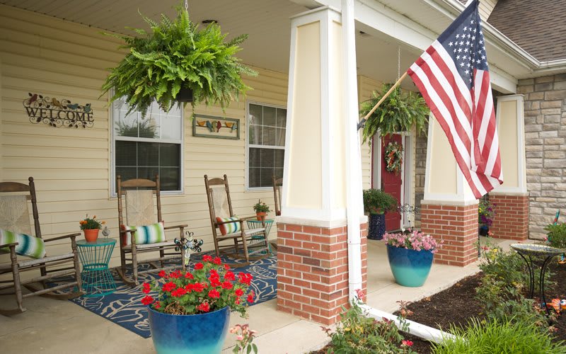 A welcoming front porch with rocking chairs, vibrant plants, and an American flag.