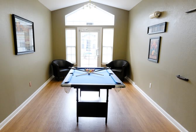A minimalist game room featuring a pool table and two chairs with a wooden floor and large window.