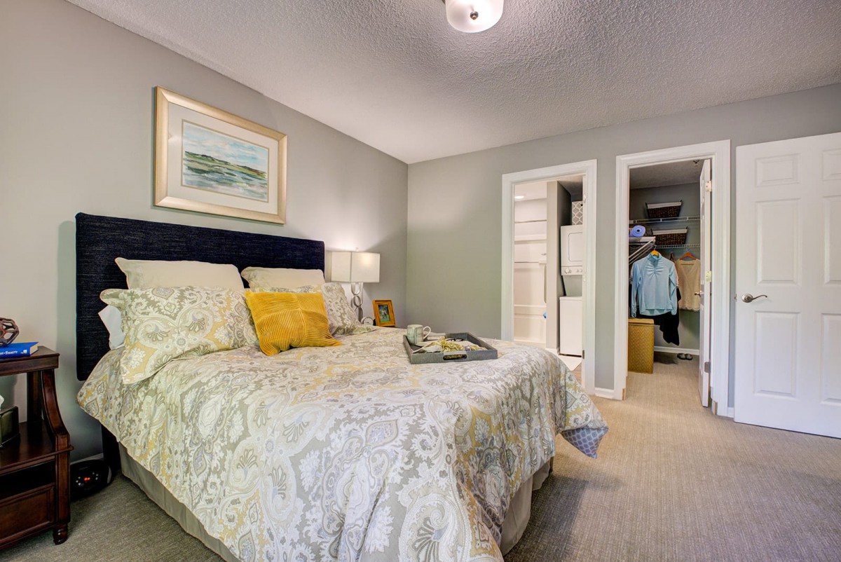 A cozy bedroom featuring a neatly made bed with decorative pillows, a nightstand with a lamp, and an open closet.