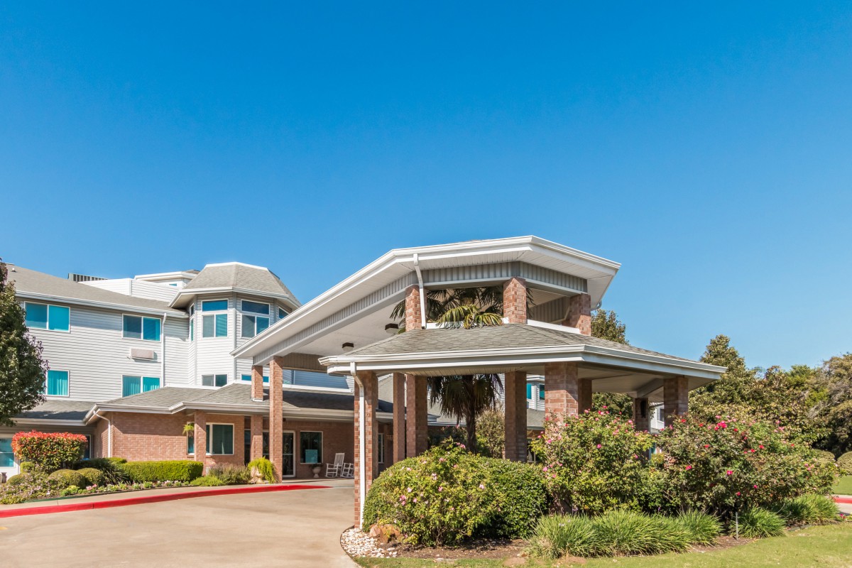 A modern residential building with a prominent entrance and landscaped surroundings under a clear blue sky.