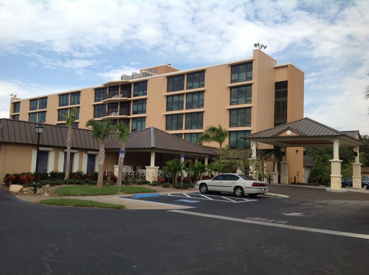 A multi-story hotel with palm trees and a car parked in the lot.