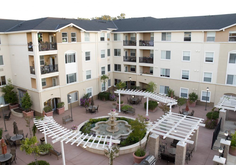 A multi-story apartment complex with a central courtyard featuring a fountain and landscaping.