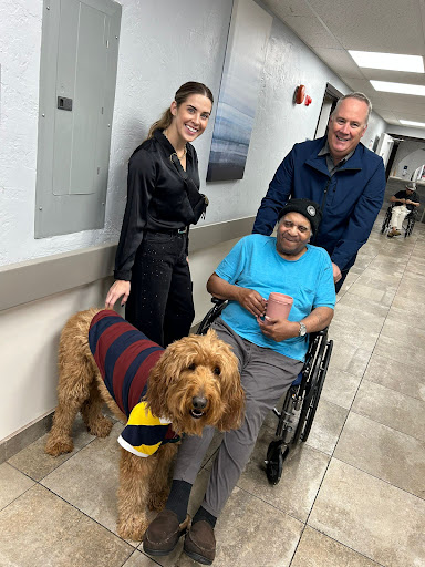 A heartwarming moment featuring a friendly dog visiting a patient in a hospital, accompanied by two supportive individuals.