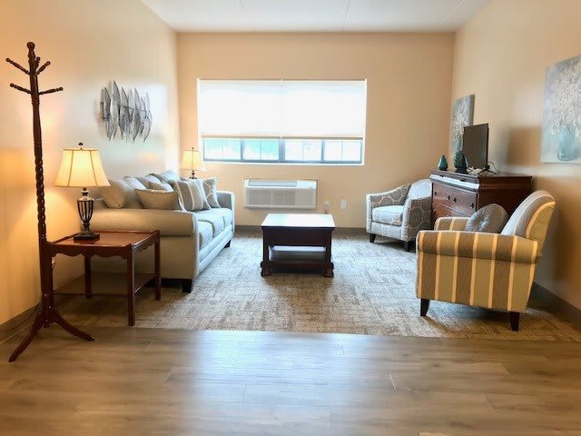 A cozy living room with a sofa, armchairs, and a coffee table, featuring a television and a window letting in natural light.