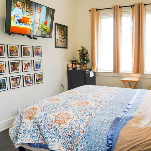 A cozy bedroom setup featuring a television, decorative photos on the wall, and warm natural lighting.