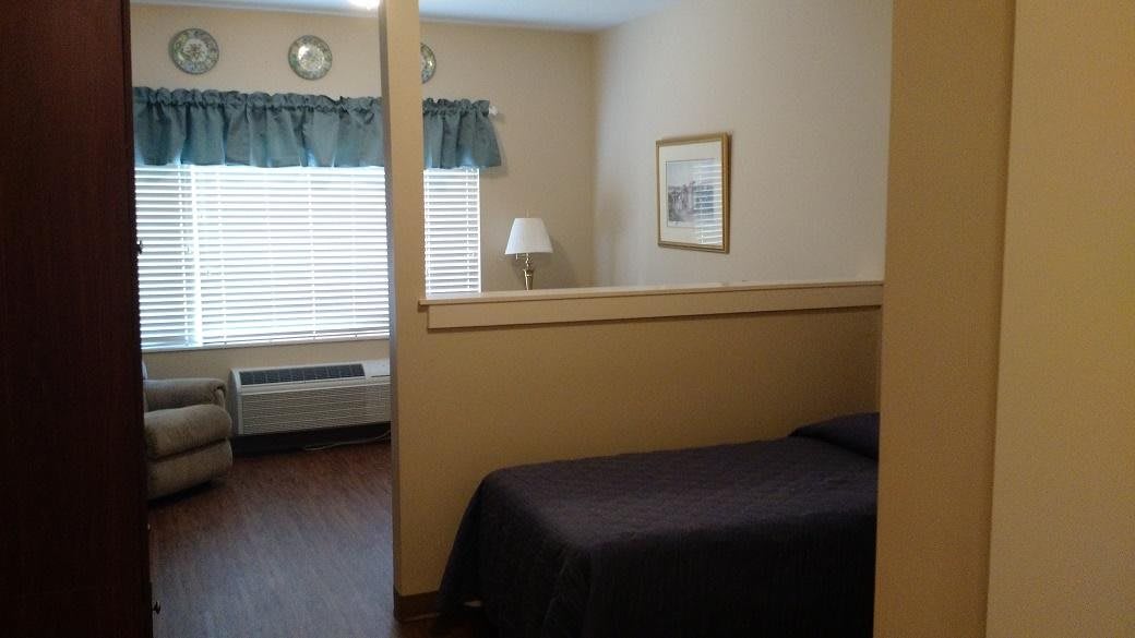 A cozy bedroom with a bed, lamp, and window with curtains.