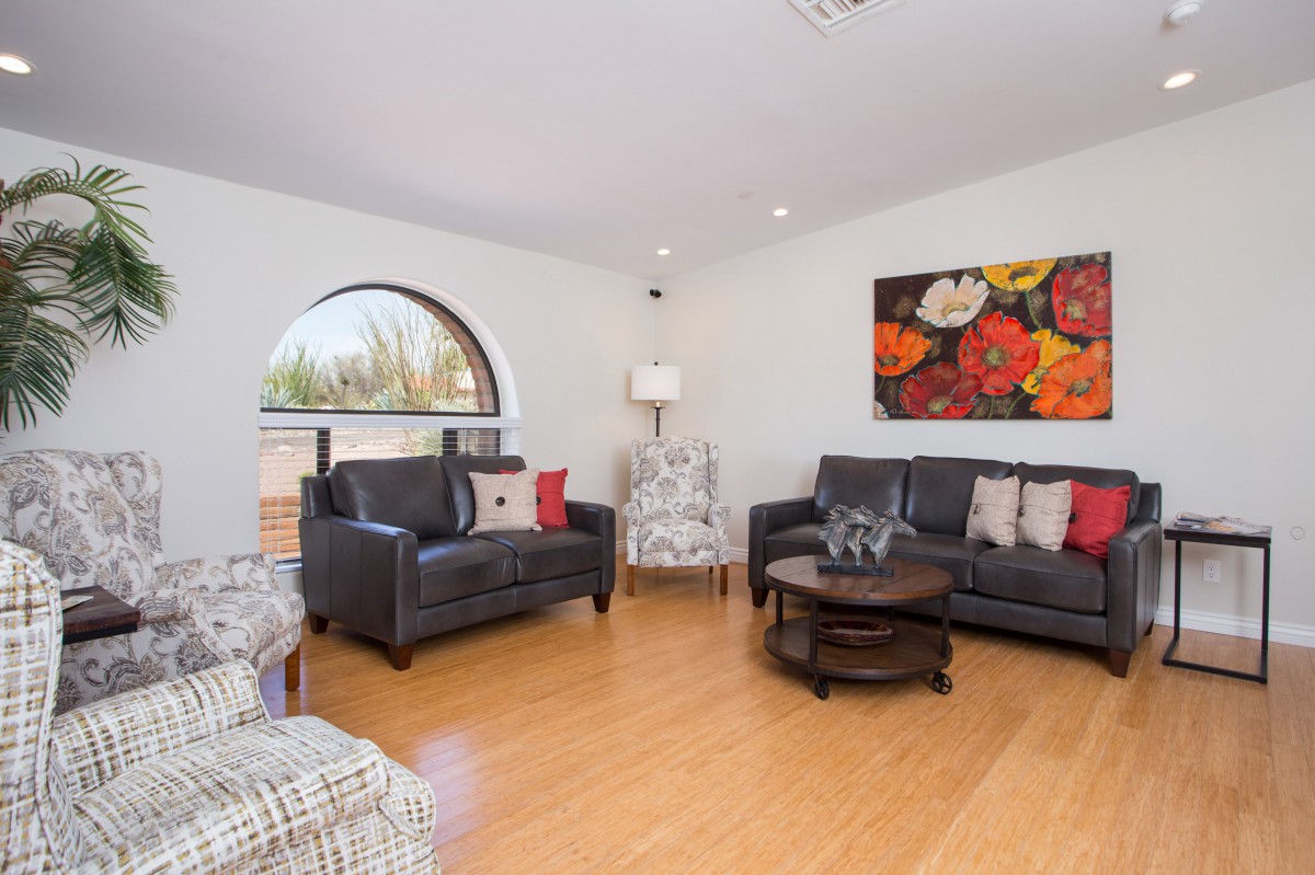 A cozy living room with modern furniture, featuring black sofas, a wooden coffee table, and colorful artwork on the wall.