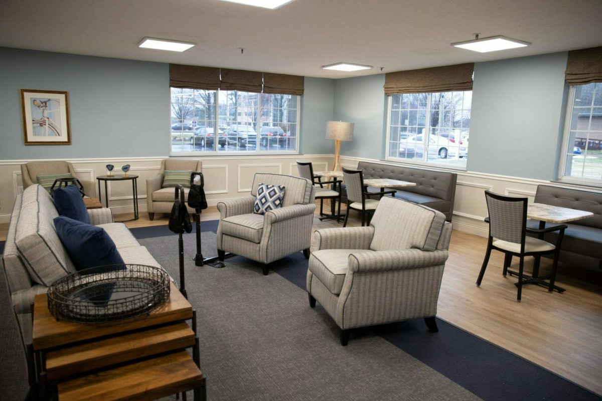 A cozy living room with chairs, a sofa, and a table, featuring large windows and a standing lamp.