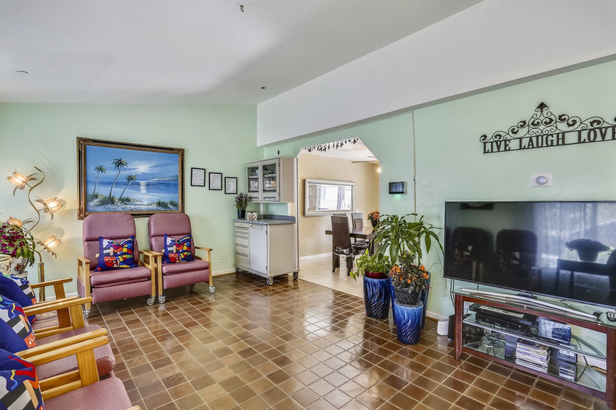 A cozy living room with a television, comfortable seating, and decorative plants.
