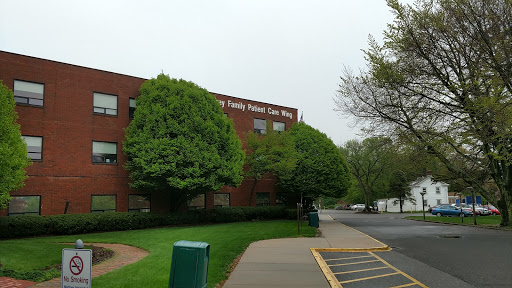 A view of a red brick building surrounded by lush greenery on a cloudy day.