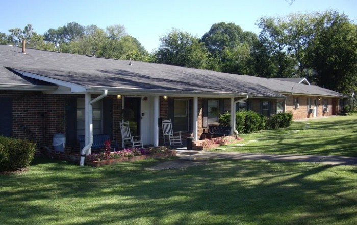 A suburban house with a porch and well-maintained lawn surrounded by trees.