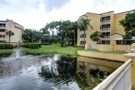 A serene view of an apartment building beside a reflective lake surrounded by lush greenery.