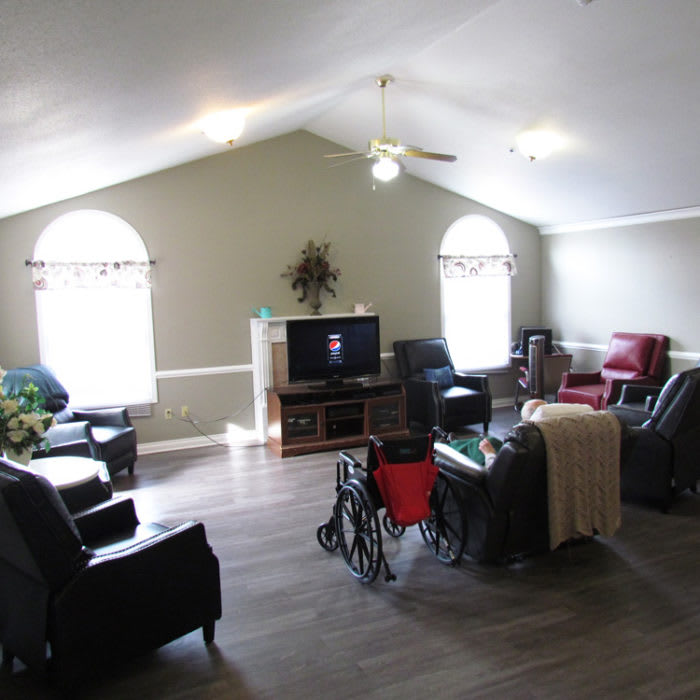 A cozy living room with various chairs, a television, large windows, and a wheelchair.