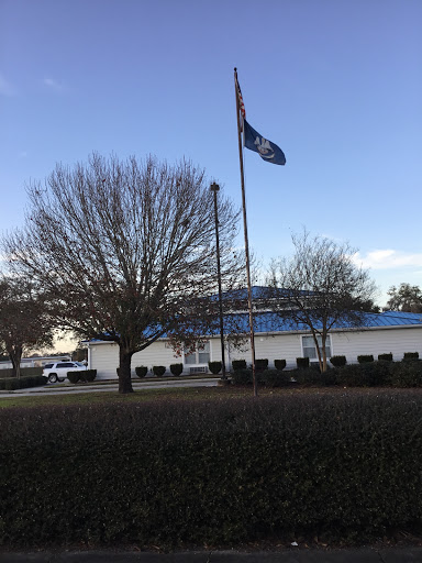 A building with a flag flying in front, surrounded by trees and a clear sky.