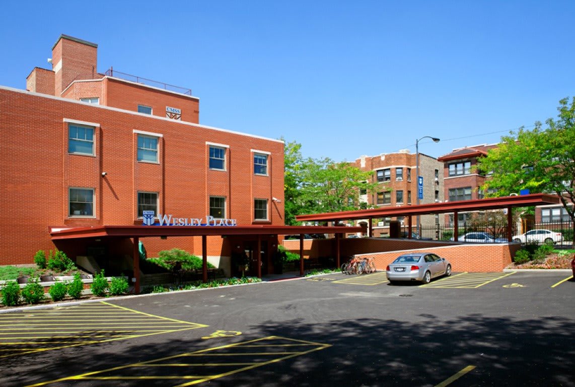 A view of a brick building with an adjacent parking lot featuring a single parked car on a sunny day.