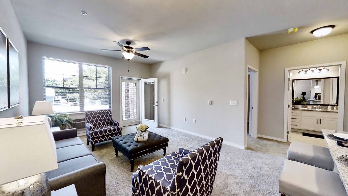 A modern living room with patterned chairs and a comfortable sofa, featuring a ceiling fan and ample natural light.