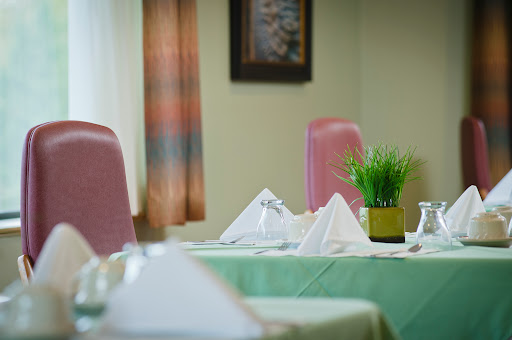 A cozy dining area featuring neatly arranged tables with green tablecloths and pink chairs, complemented by decorative plants.