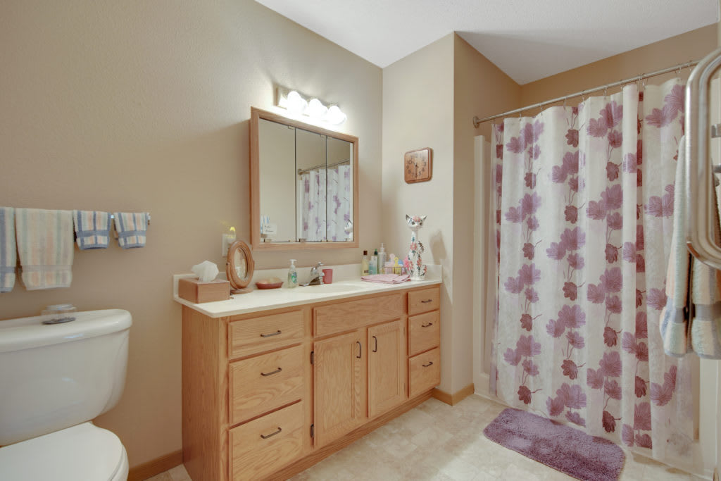 A well-organized bathroom with a wooden vanity, mirror, and floral shower curtain.