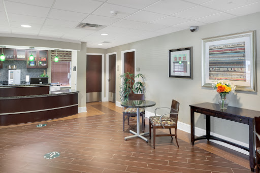 A modern office waiting area featuring a reception desk, seating, and decorative plants.