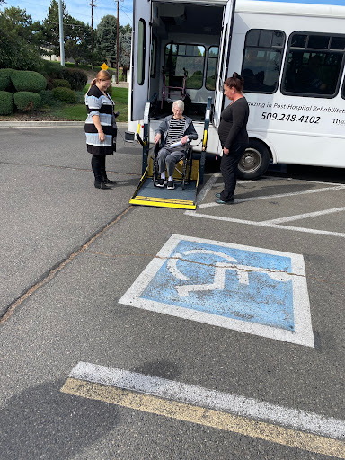 A scene depicting two individuals assisting a person in a wheelchair onto a bus equipped with a ramp.
