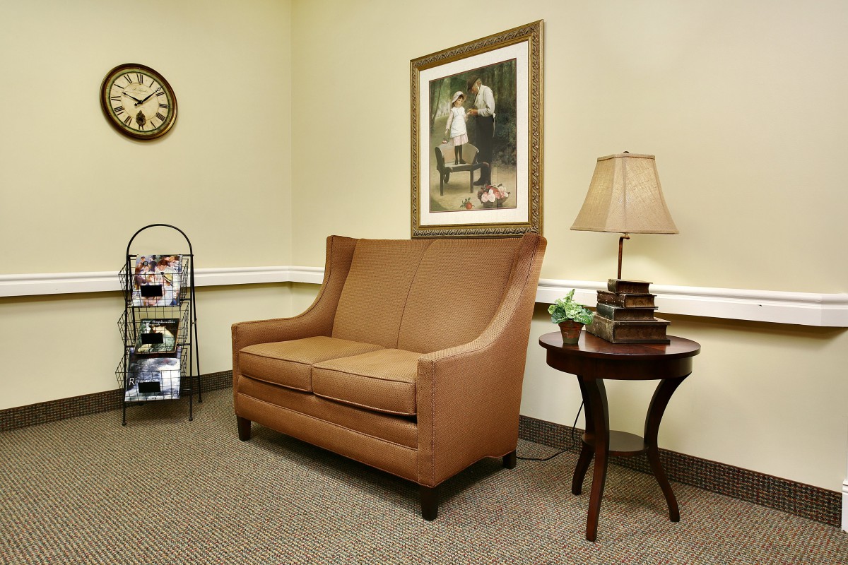 A cozy waiting room with a brown sofa, side table, and decorative lamp.