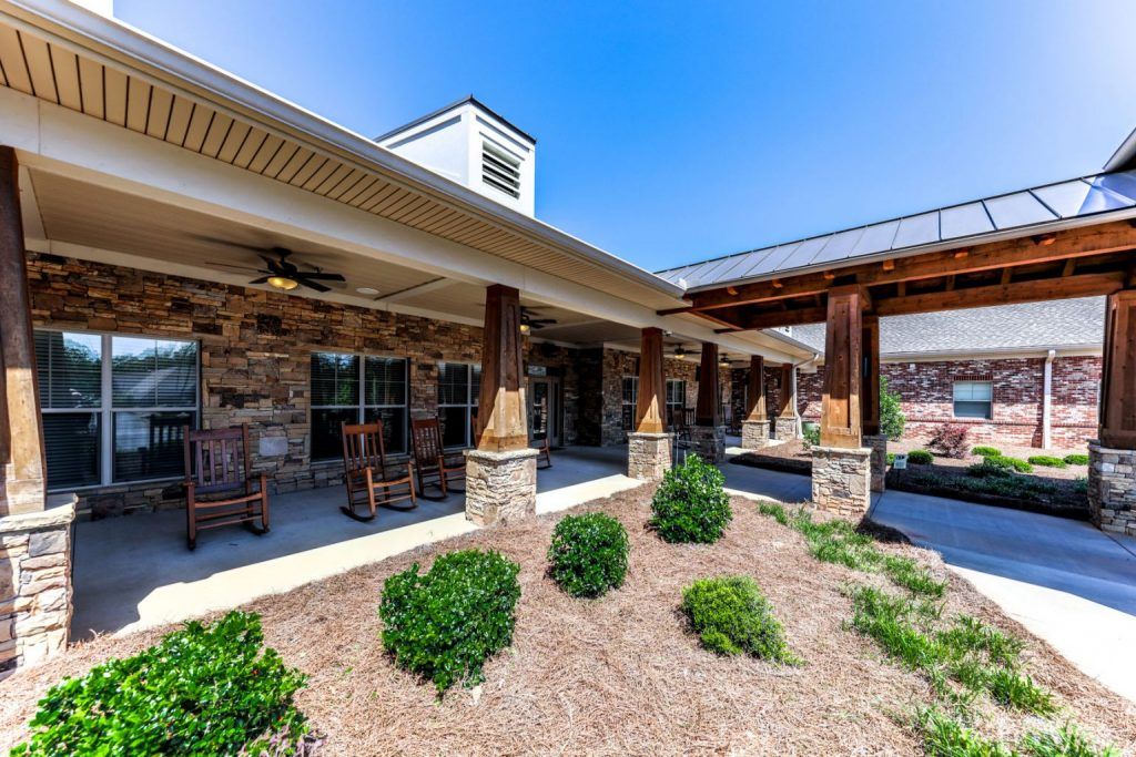 A rustic-style building with a stone facade and wooden pillars, featuring a landscaped area with shrubs.