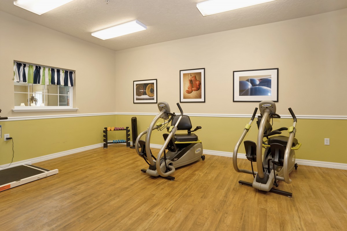 A small gym room with exercise equipment and wooden flooring.