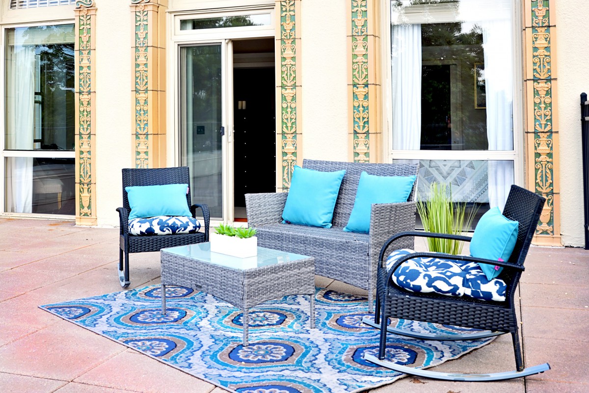 A stylish outdoor patio setup featuring a sofa, chairs, and a table with blue accents and a patterned rug.