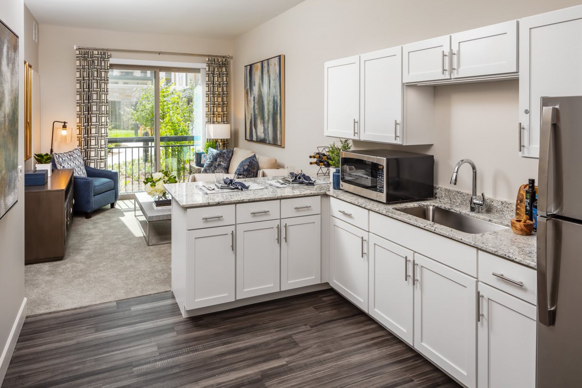 A modern open-layout apartment featuring a kitchen with white cabinets and a connected living room.