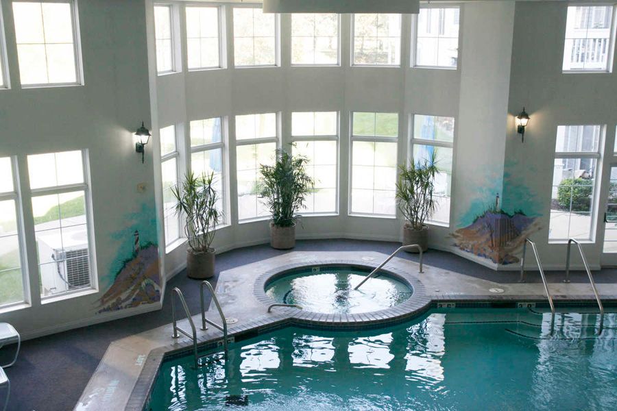 A luxurious indoor pool and hot tub area with large windows and decorative plants.
