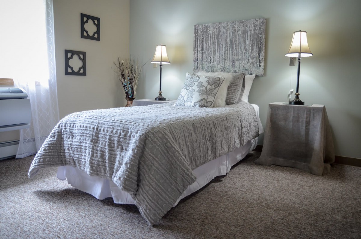 A cozy bedroom with a neatly made single bed, soft lighting from lamps, and elegant wall art.