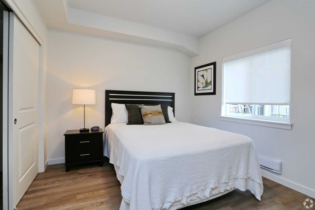 A minimalist bedroom with a neatly made bed, a nightstand with a lamp, and simple decor.