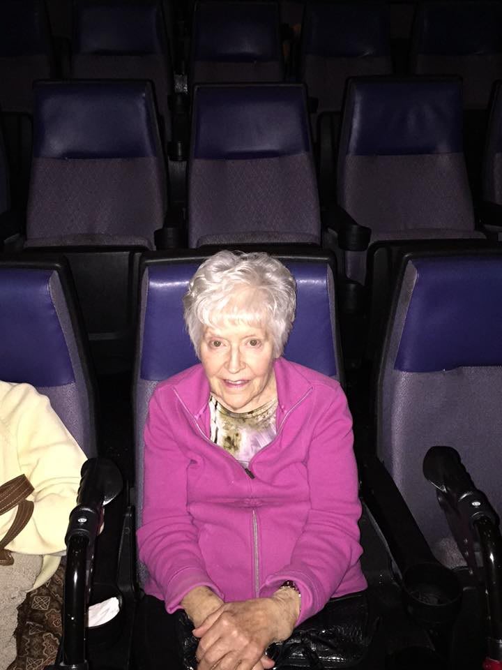 An elderly woman sitting in a mostly empty movie theater.