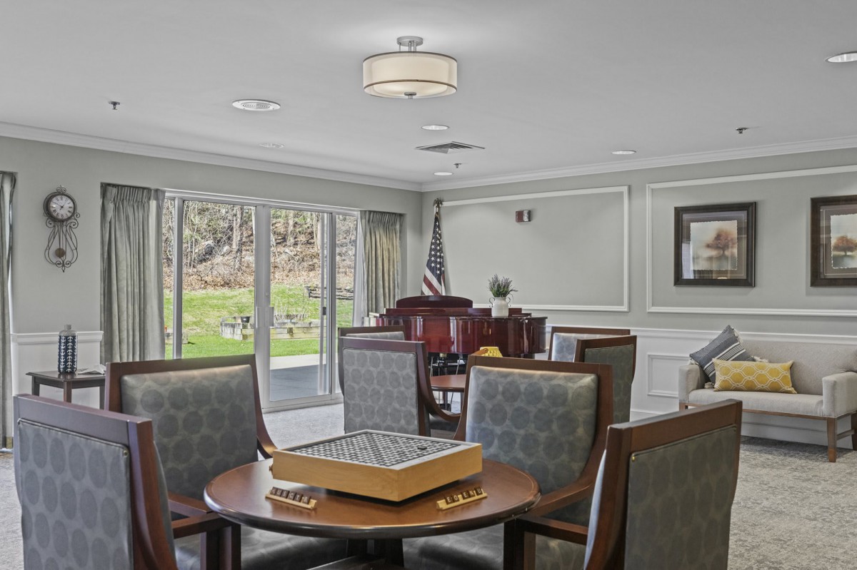 A well-furnished living room with a game table and comfortable seating, overlooking a garden view through large windows.