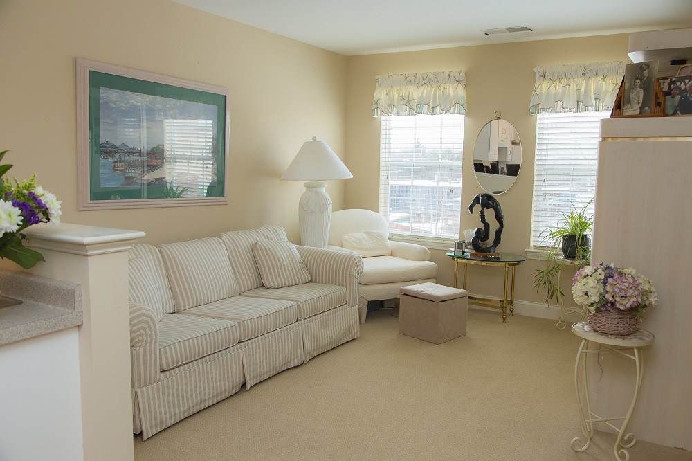 A cozy living room featuring a white sofa, table lamp, and decorative elements with large windows providing natural light.