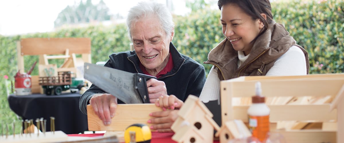 An elderly man and a woman working together on a woodworking project, building birdhouses.