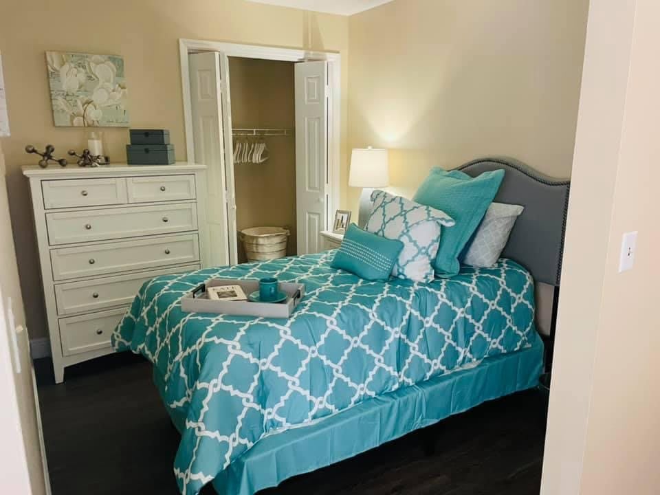 A cozy bedroom with a teal and white patterned bedspread, matching pillows, and a bedside lamp.