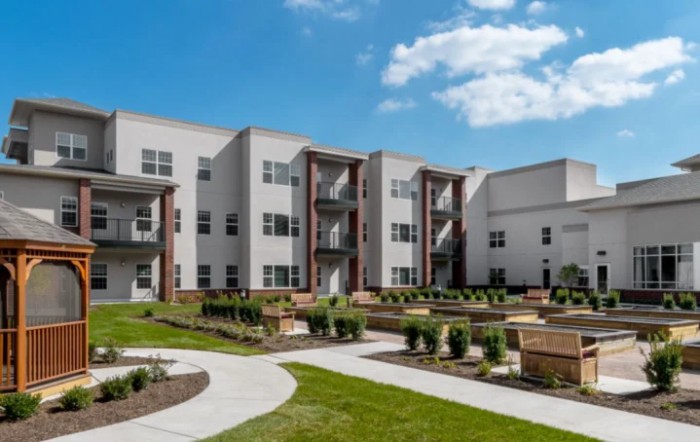 A modern apartment complex with well-maintained landscaping under a clear blue sky.