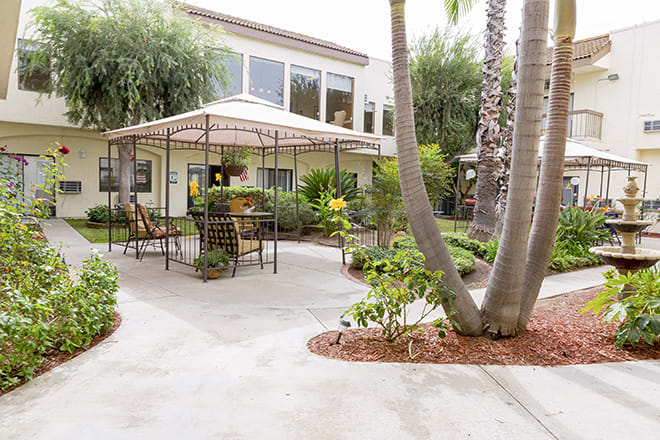 A peaceful garden patio with a gazebo and seating area surrounded by lush greenery.