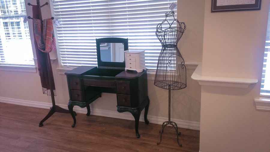 A vintage vanity table with a mirror and a dress form beside it in a well-lit room.