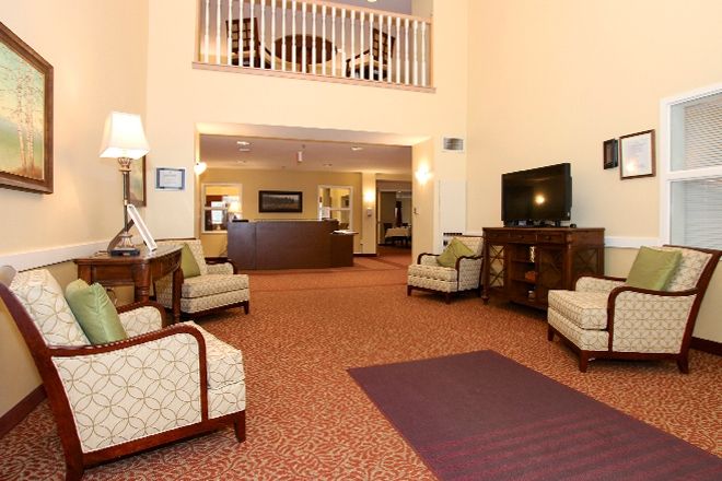 A spacious hotel lobby with comfortable seating, a television, and a reception desk in the background.