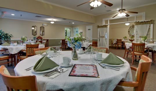 A neatly set dining table in a restaurant with green napkins and floral centerpiece.