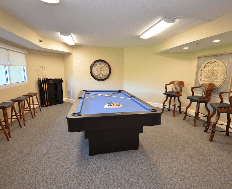 A cozy game room with a pool table and bar stools.