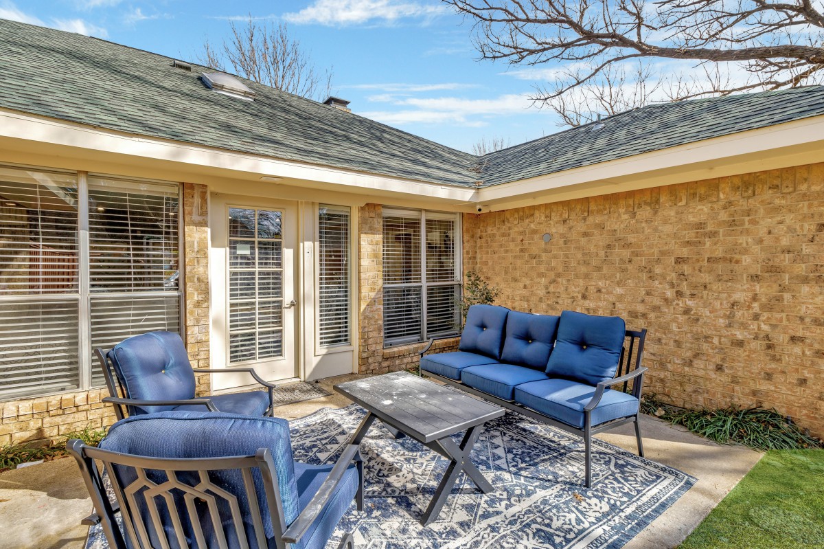 A cozy patio area with blue outdoor furniture and a patterned rug against a brick house.