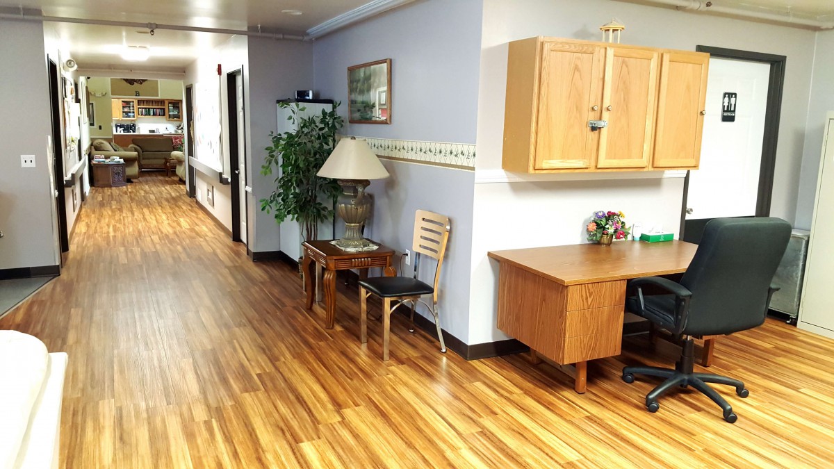 A well-lit hallway with wooden flooring, featuring office furniture and indoor plants.