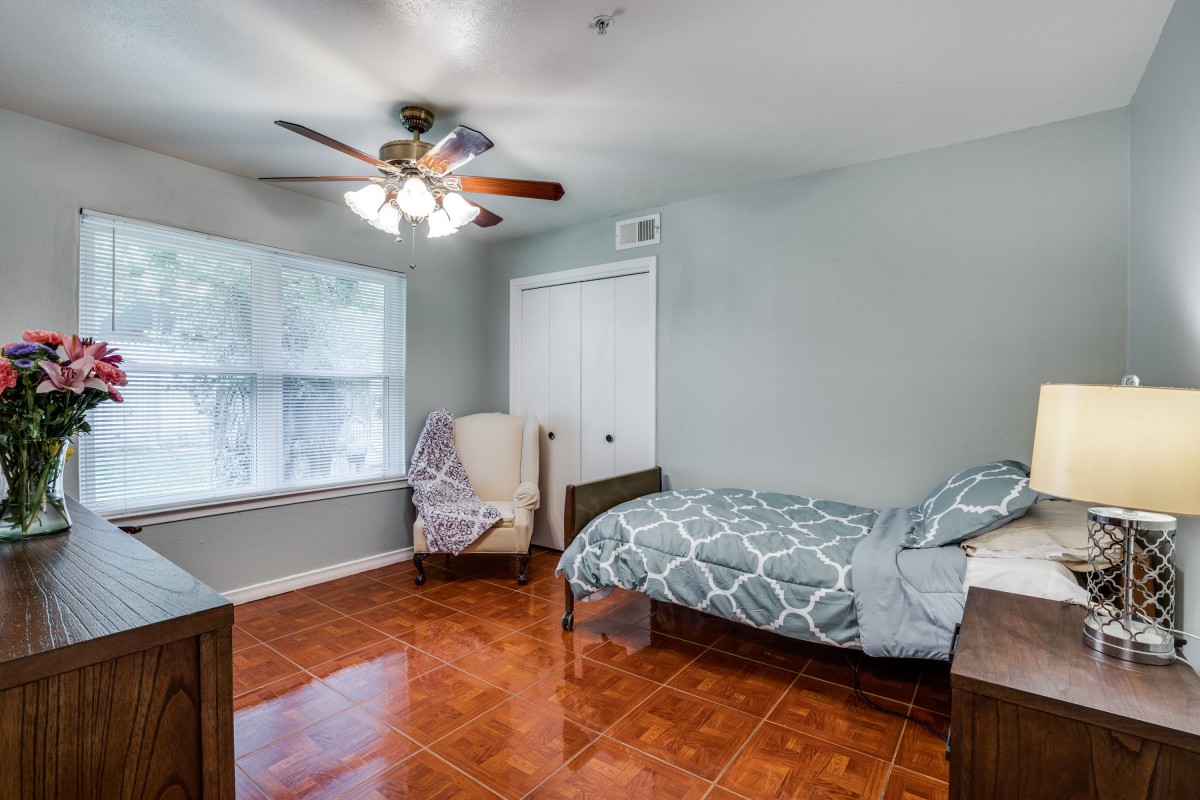 A cozy bedroom with a single bed, armchair, and ceiling fan.
