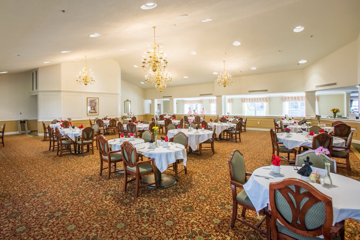 An elegant dining room with neatly arranged tables and chairs, adorned with chandeliers.