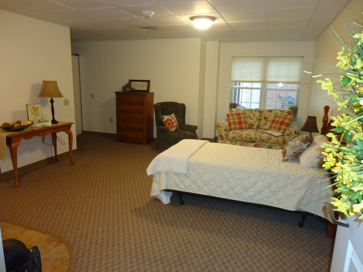 A spacious bedroom with a bed, sofa, chest of drawers, and chair.