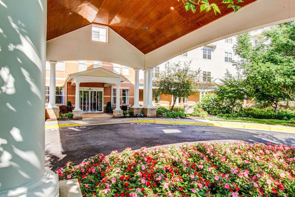 A beautifully landscaped building entrance with a covered walkway and vibrant flower beds.